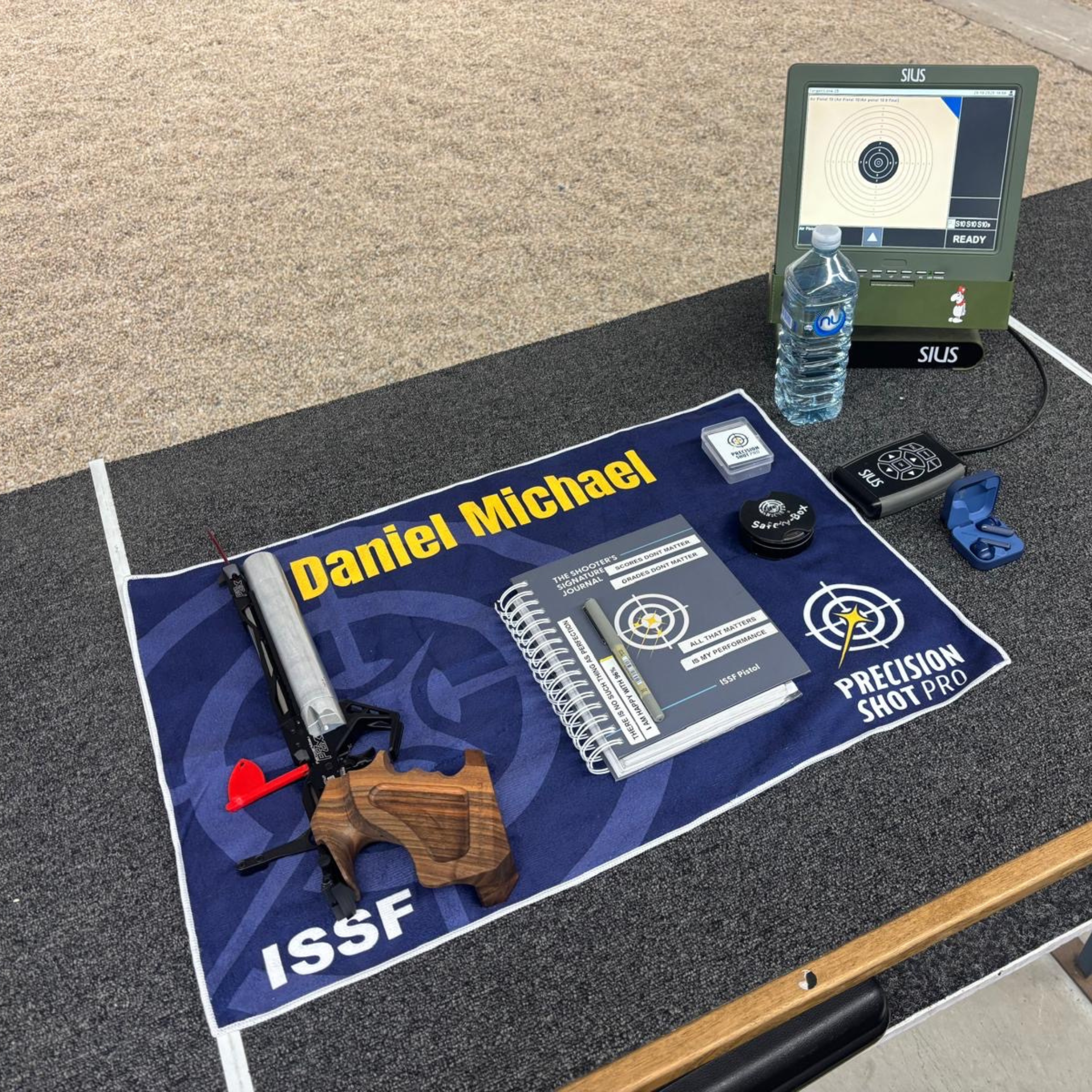 PSP custom name range towel on a 10m air pistol bench, with an air pistol, a shooting journal and shooting accessories on top