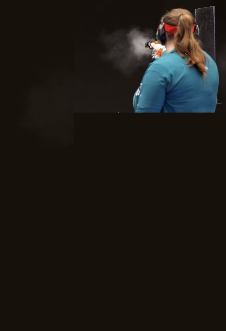ISSF woman shooting 25m pistol with muzzle smoke on a black background.