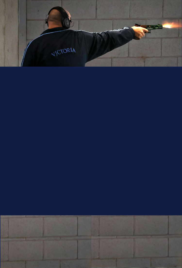 ISSF pistol shooter on indoor range firing shot with muzzle flash, mobile banner crop with navy lower section.